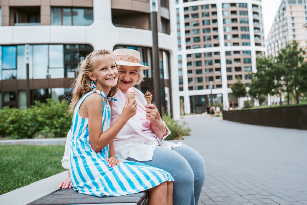 Grandma and granddaugter in the city, sitting on bench. Girl spending time with senior grandmother, during holidays, after school.