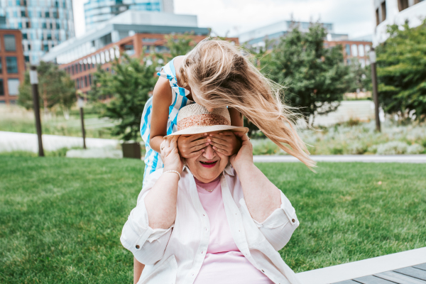 Girl covering grandma's eyes with hands. Granddaughter spending time with senior grandmother, during summer break or after school.