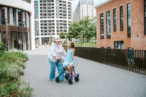 Grandma with walker and granddaugter in the city, on walk. Girl spending time with senior grandmother, during holidays, after school.