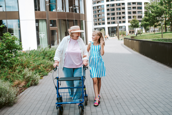 Grandma with walker and granddaugter in the city, on walk. Girl spending time with senior grandmother, during holidays, after school.