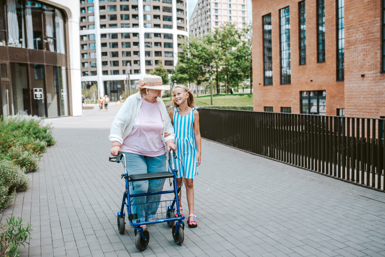 Grandma with walker and granddaugter in the city, on walk. Girl spending time with senior grandmother, during holidays, after school.