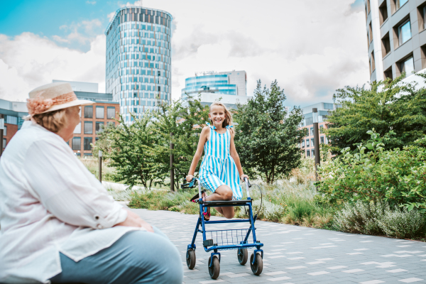 Grandma having fun with granddaugter in the city. Girl sitting on walker, spending time with senior grandmother, during summer break or after school.