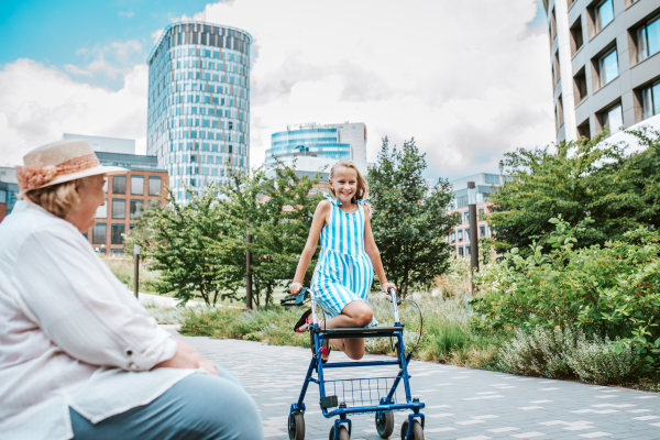 Grandma having fun with granddaugter in the city. Girl sitting on walker, spending time with senior grandmother, during summer break or after school.