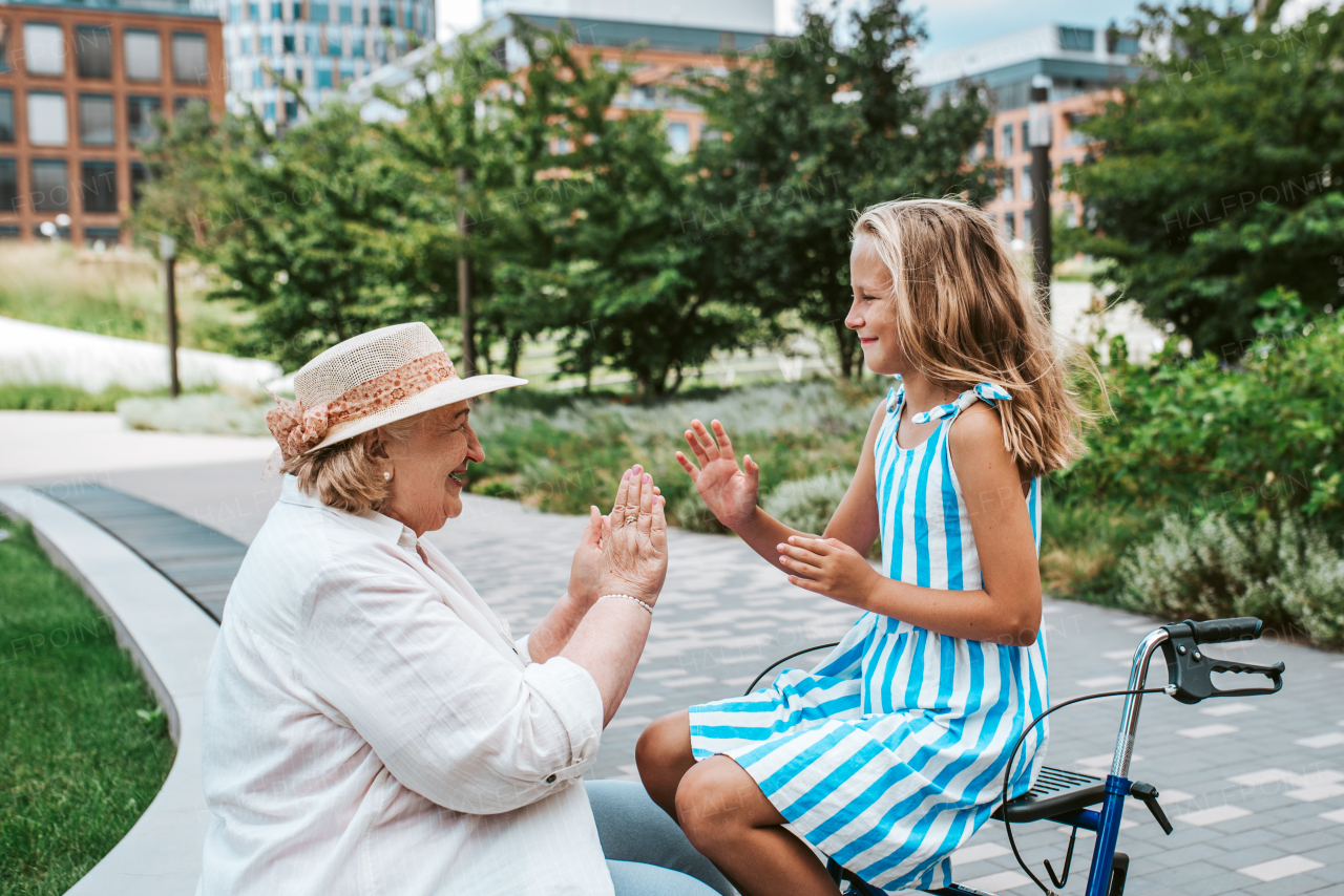 Grandma having fun with granddaugter in the city. Girl sitting on walker, spending time with senior grandmother, during summer break or after school.