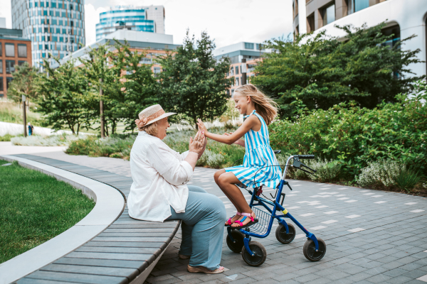 Grandma having fun with granddaugter in the city. Girl sitting on walker, spending time with senior grandmother, during summer break or after school.