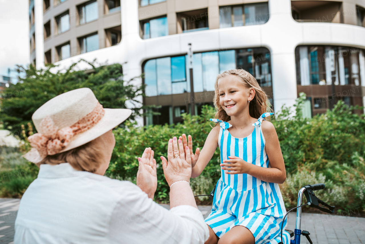 Grandma having fun with granddaugter in the city. Girl sitting on walker, spending time with senior grandmother, during summer break or after school.