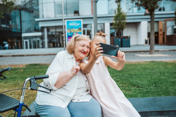 Grandma taking selfie with granddaugter sitting on bench. Girl spending time with senior grandmother, during summer break or after school.