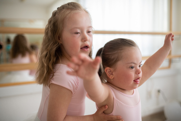 Little sisters with down syndrome dancing ballet in a ballet school studio.