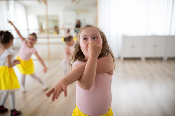 Little girl with down syndrome imitating an elephant, having fun during ballet leson at dancing school.