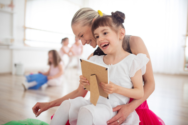 Happy disabled girl cuddling with her mother and looking at a photo during ballet class. Concept of integration disabled children and parenthood.