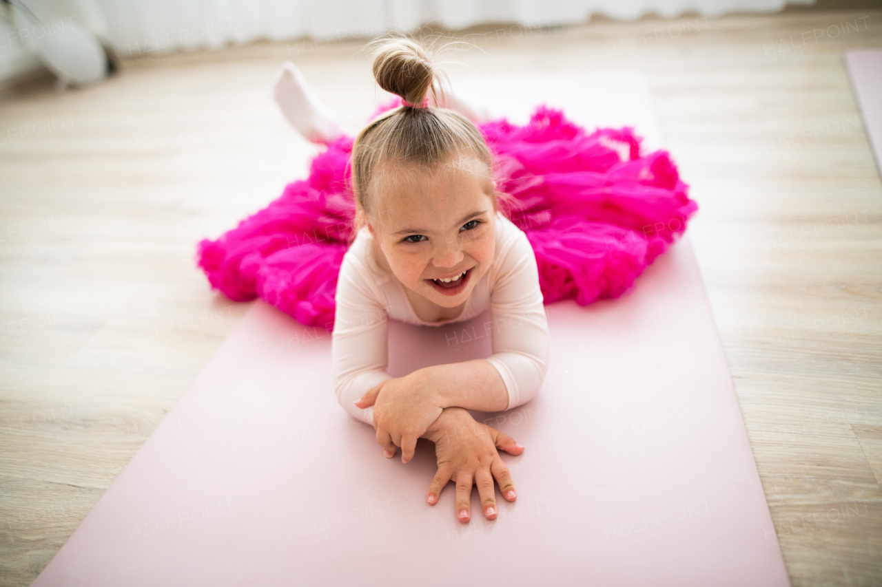 Little girl with down syndrome at a ballet class in dance studio, lying and resting. Concept of integration and education of disabled children.