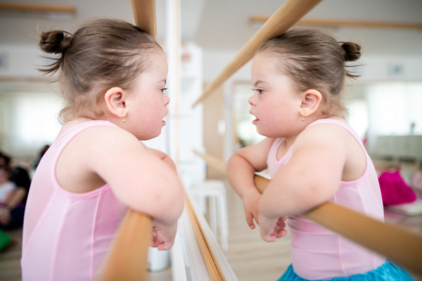 Little girl with down syndrome at a ballet class in dance studio,standing in front of mirror. Concept of integration and education of disabled children.