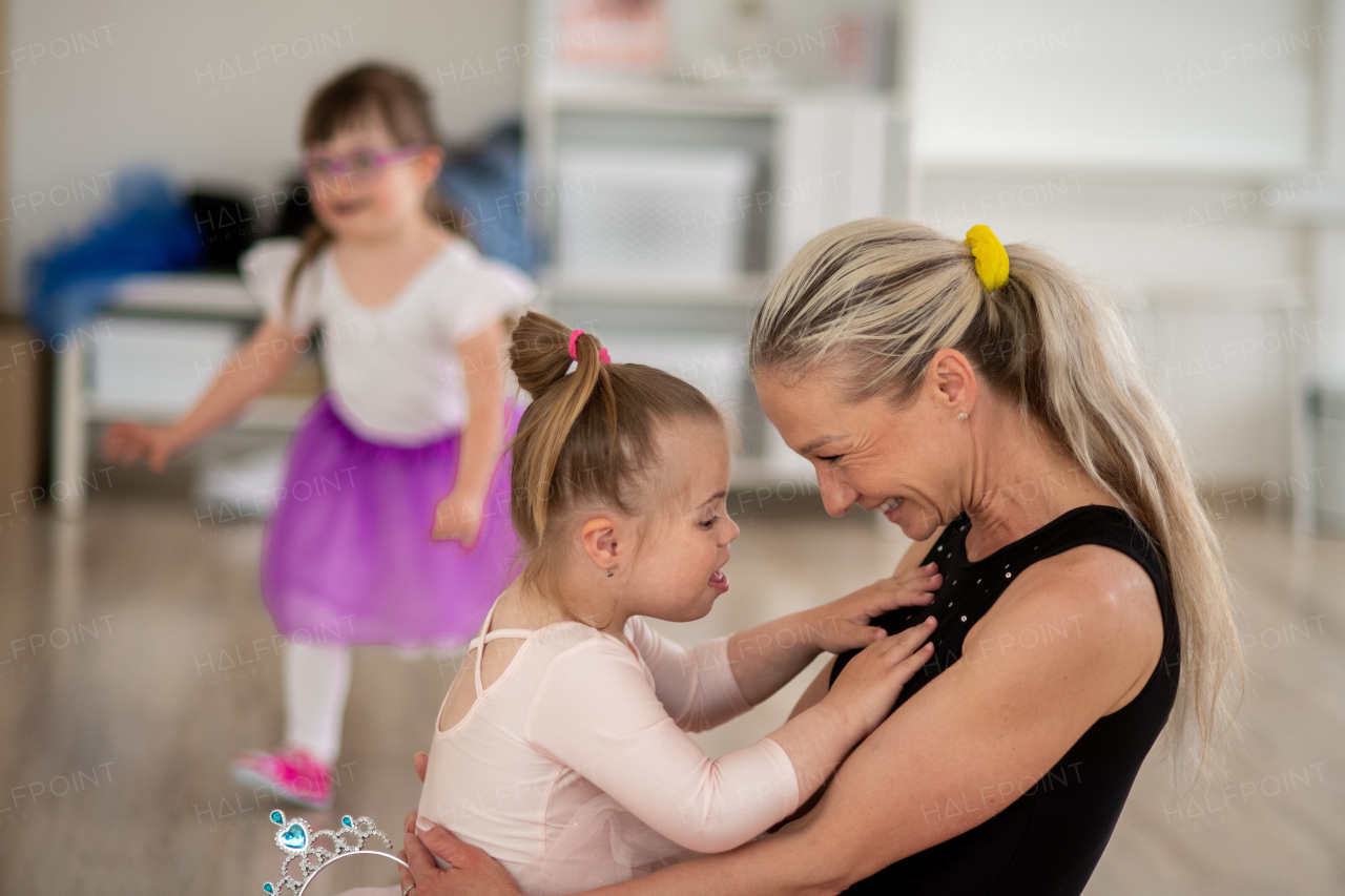 Little girl with down syndrome cuddling with her mother during ballet class. Concept of disabled children and their parenthood.