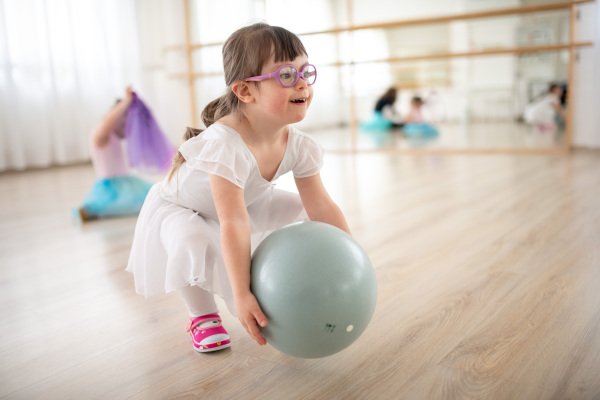 Little girl with down syndrome playing with ball at a ballet class in dance studio. Concept of integration and education of disabled children.