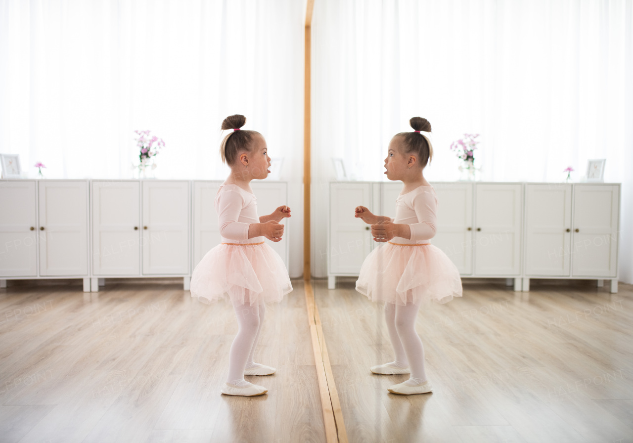 Little girl with down syndrome at a ballet class in dance studio,standing in front of mirror. Concept of integration and education of disabled children.