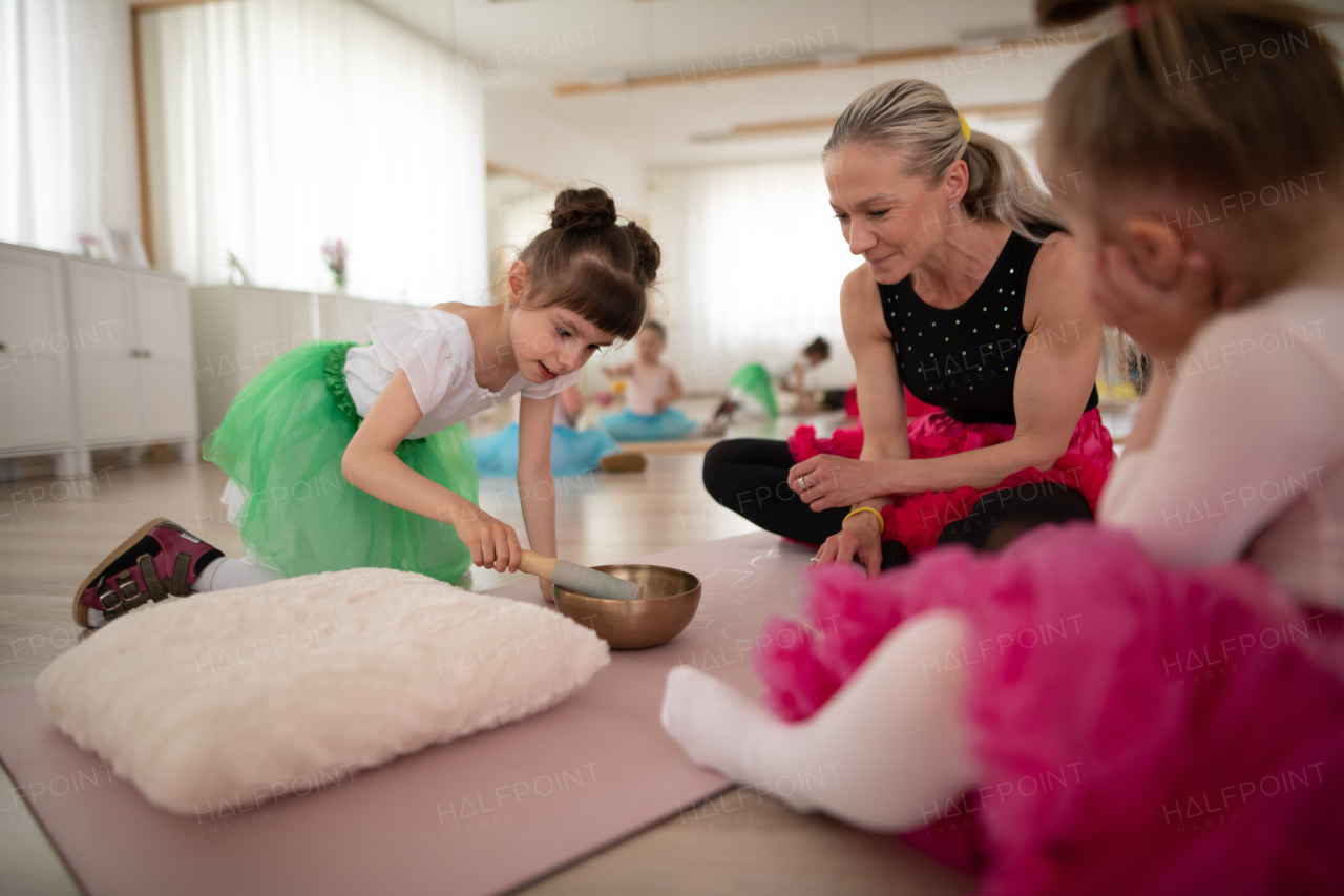 Little dissabled girls with their lecteur sitting on the floor in ballet dancing studio and making sound on a tibetian singing bowl.