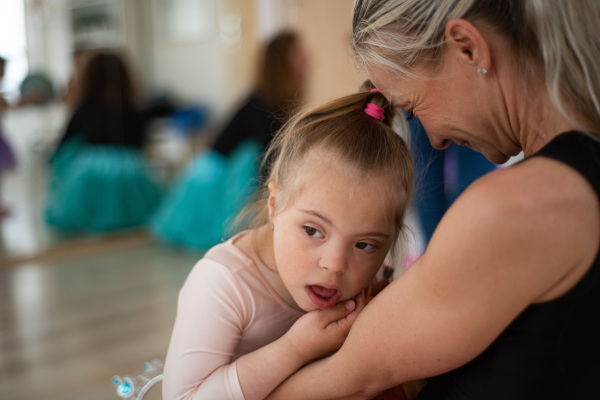 Little girl with down syndrome waiting for a ballet class with her mother. Concept of integration disabled children and parenthood.