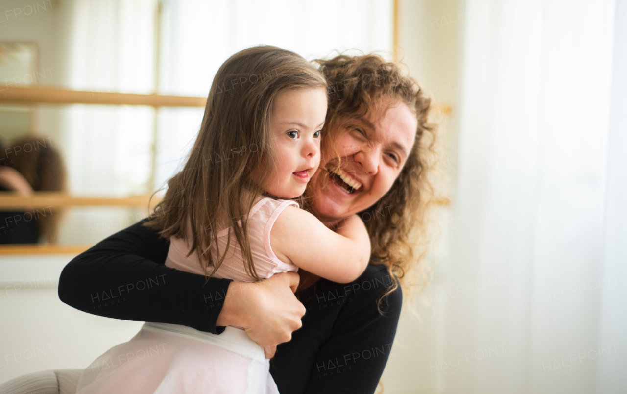 Young happy mother holding her daughter with down syndome, having fun in a ballet dance studio, concept of education and integration dissabled children.