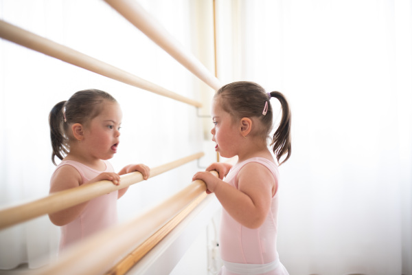 Little girl with down syndrome at a ballet class in dance studio,standing in front of mirror. Concept of integration and education of disabled children.