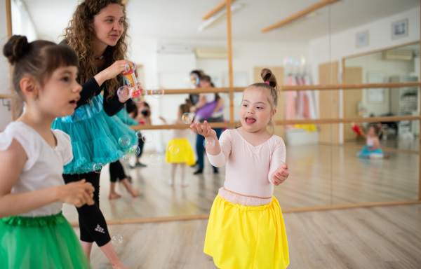 Little girls with down syndrome and dance lecturer having fun in a ballet school studio.