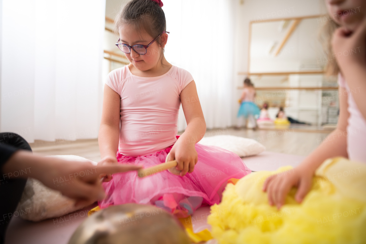 Little girls with down syndrom sitting on the floor in a ballet dancing studio and making sound on a tibetian singing bowl.