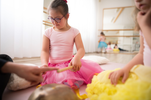 Little girls with down syndrom sitting on the floor in a ballet dancing studio and making sound on a tibetian singing bowl.