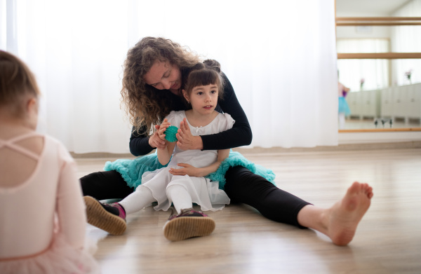 Young ballet lecteur doing hand massage with a special ball to little disabled girl.