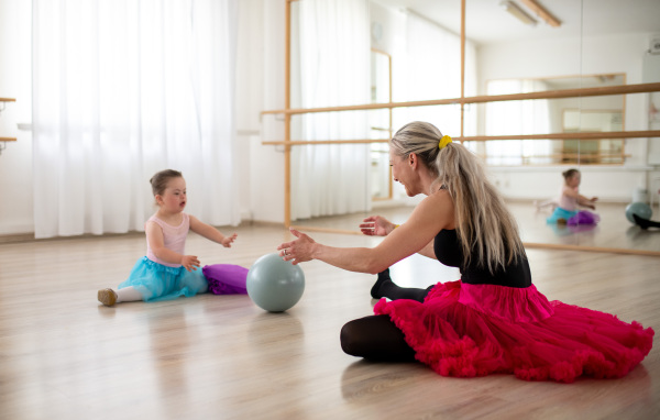 Little girl with down syndrome playing with a ball with her dance lecteur in ballet studio.