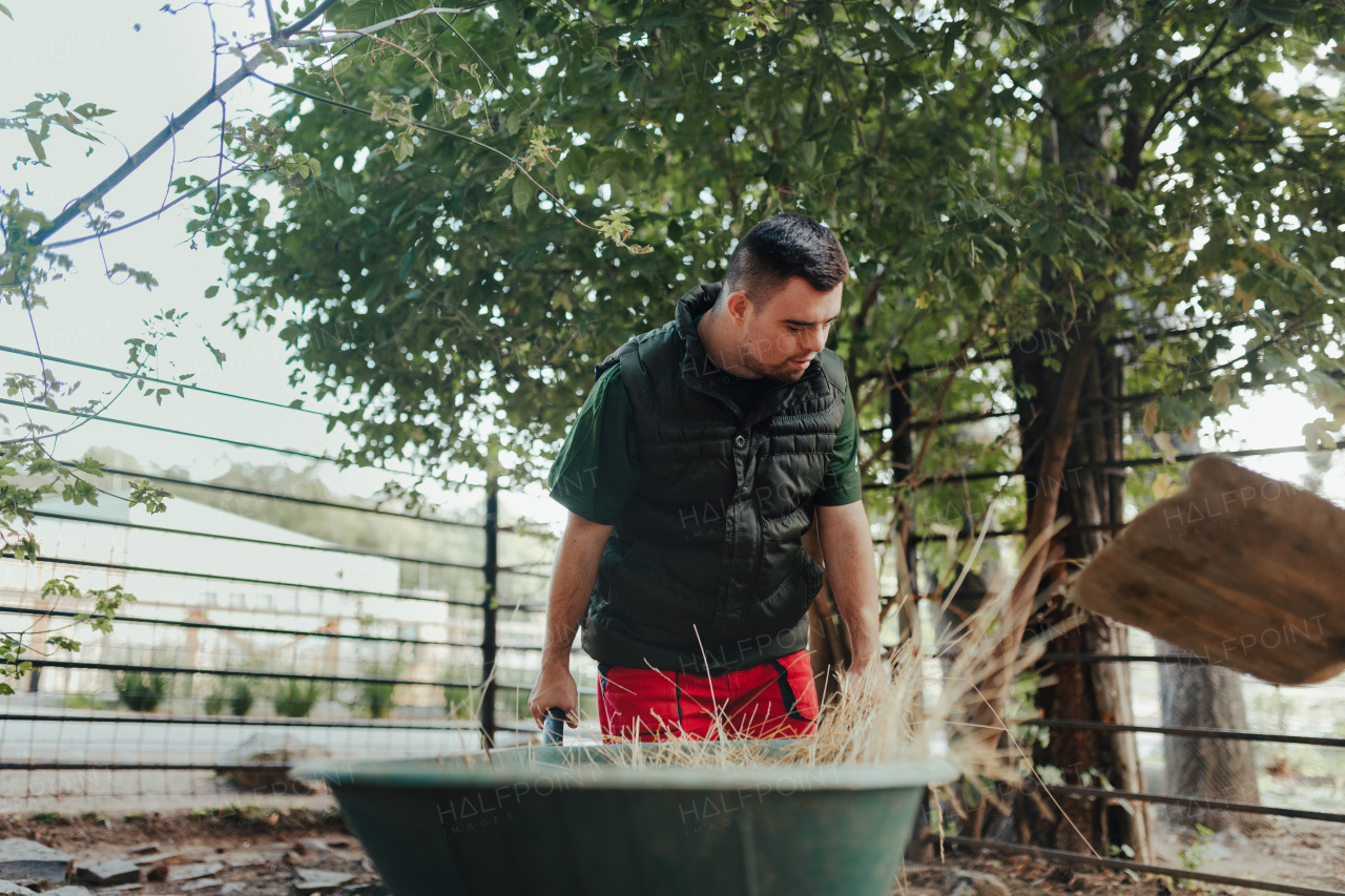 Caretaker with down syndrome in the cleaning animal enclosure. Concept of integration people with disabilities into society.