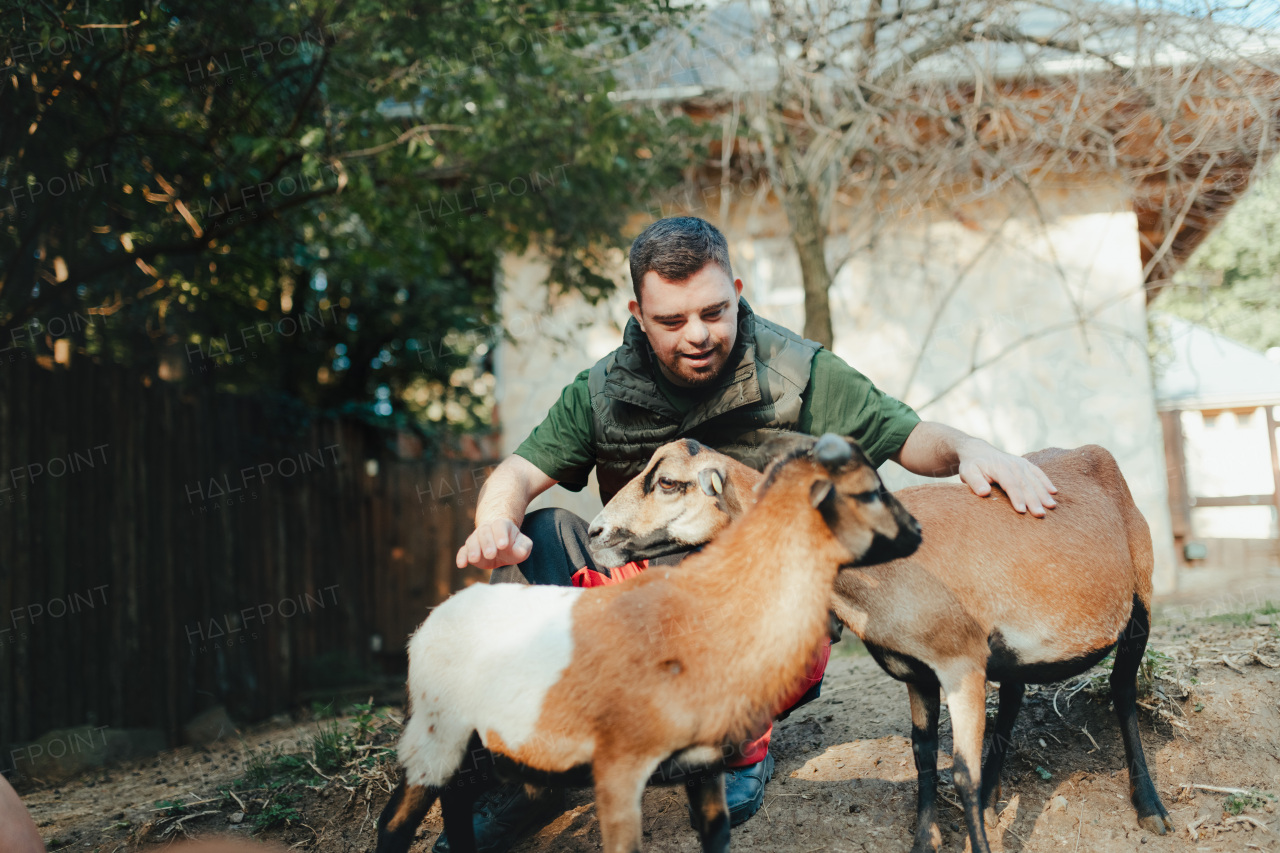 Caretaker with down syndrome taking care of animals in zoo, stroking a goats. Concept of integration people with disabilities into society.