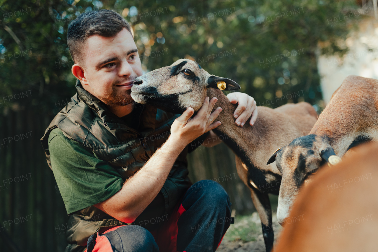 Caretaker with down syndrome taking care of animals in zoo, stroking a goat. Concept of integration people with disabilities into society.