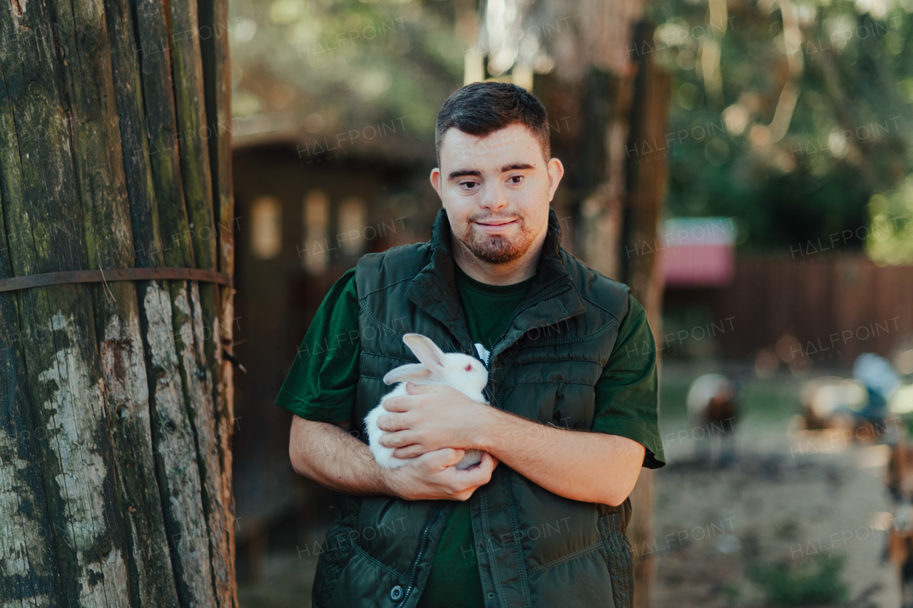 Caretaker with down syndrome taking care of animals in zoo, stroking a rabbit. Concept of integration people with disabilities into society.