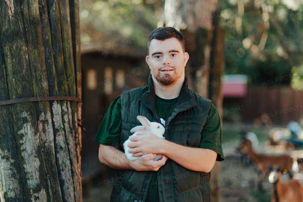 Caretaker with down syndrome taking care of animals in zoo, stroking a rabbit. Concept of integration people with disabilities into society.