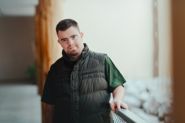 Portrait of pensive man with down syndrome, resting after cleaning animal enclosure in zoo. Concept of integration people with disabilities into society.