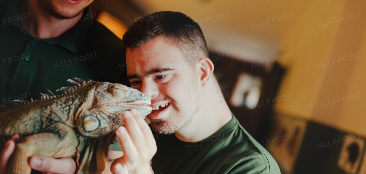 Caretaker with down syndrome taking care of animals in zoo, stroking an iguana. Concept of integration people with disabilities into society.