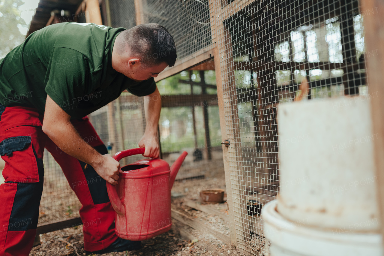 Caretaker with down syndrome in the zoo giving water in animal enclosure. Concept of integration people with disabilities into society.