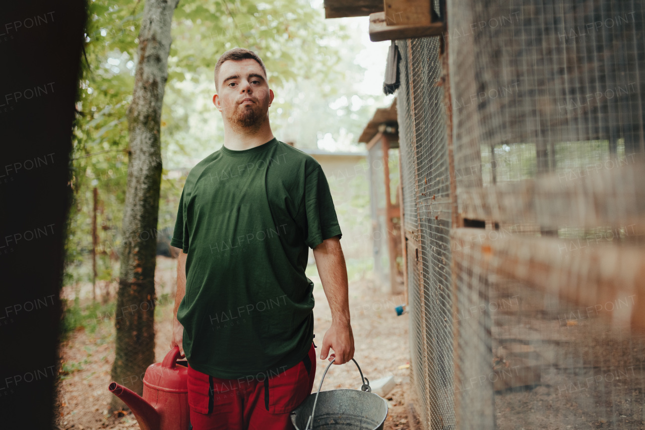 Caretaker with down syndrome in the cleaning animal enclosure. Concept of integration people with disabilities into society.