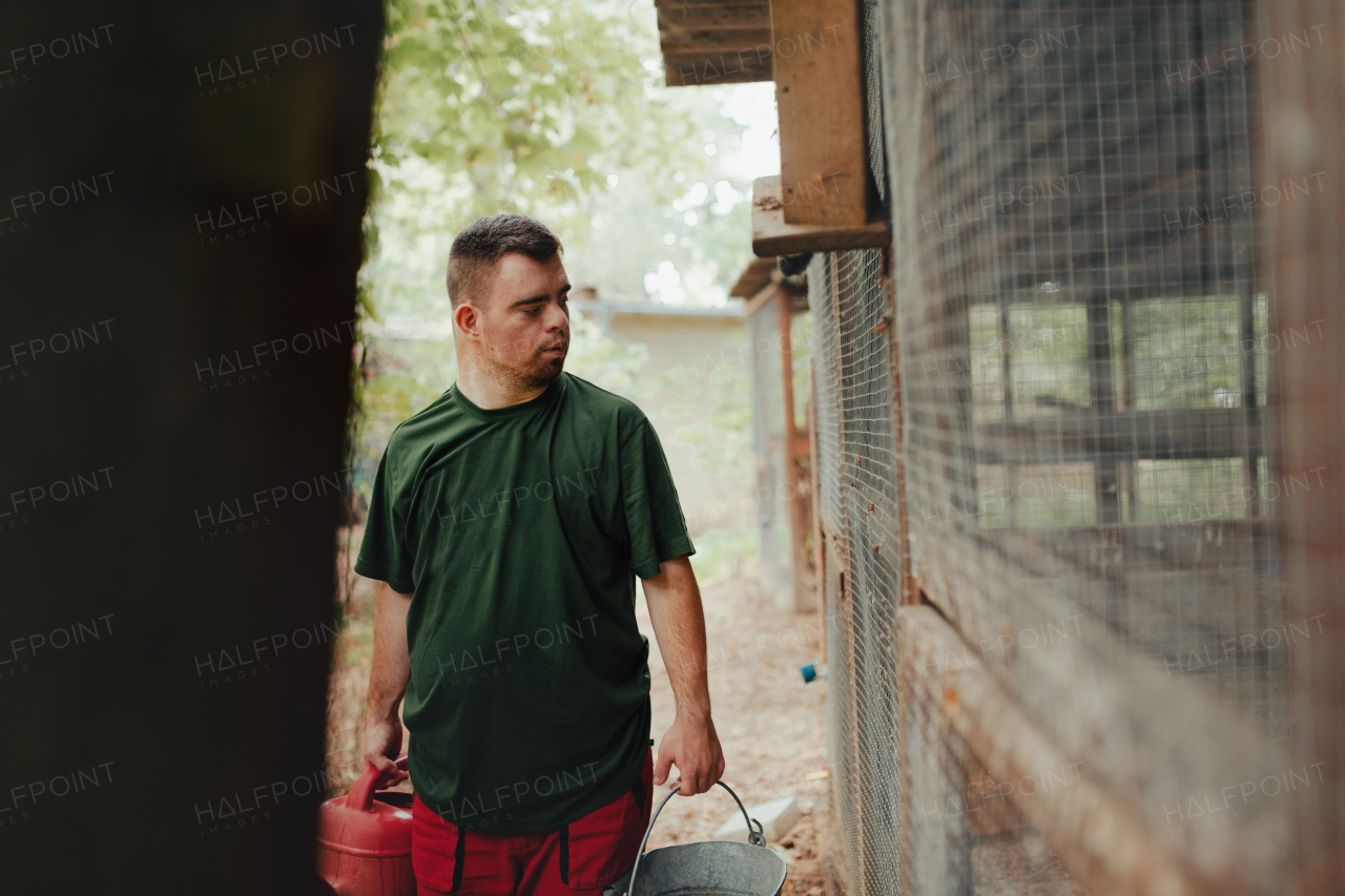 Caretaker with down syndrome in the zoo giving water in animal enclosure. Concept of integration people with disabilities into society.