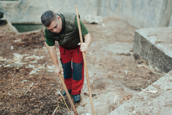 Caretaker with down syndrome in the cleaning animal enclosure. Concept of integration people with disabilities into society.