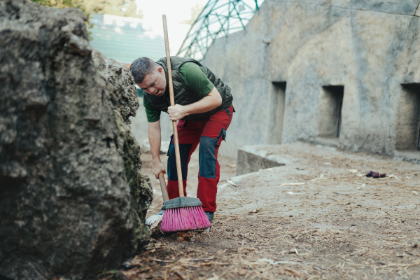 Caretaker with down syndrome in the cleaning animal enclosure. Concept of integration people with disabilities into society.