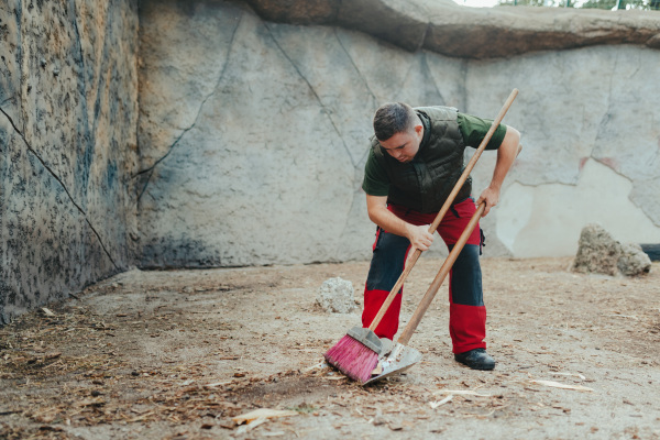 Caretaker with down syndrome in the cleaning animal enclosure. Concept of integration people with disabilities into society.