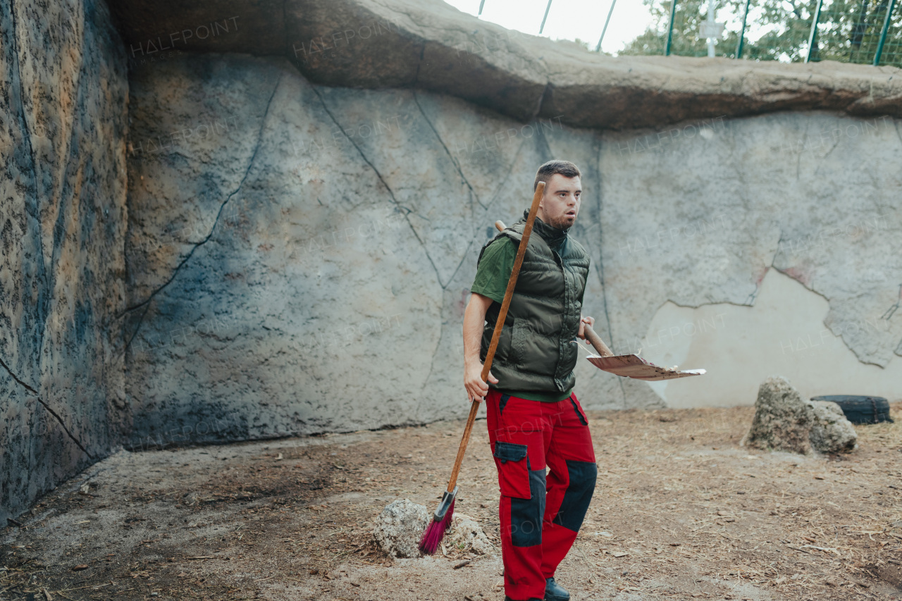 Caretaker with down syndrome in the cleaning animal enclosure. Concept of integration people with disabilities into society.