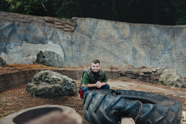 Young man with down syndrome, resting after cleaning animal enclosure in the zoo. Concept of integration people with disabilities into society.