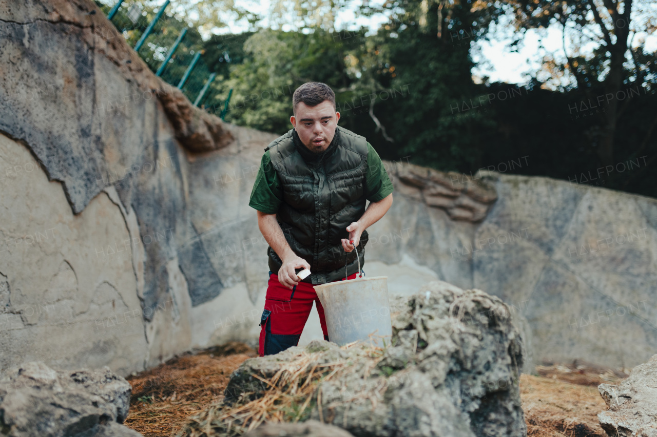 Caretaker with down syndrome in the giving food in animal enclosure. Concept of integration people with disabilities into society.