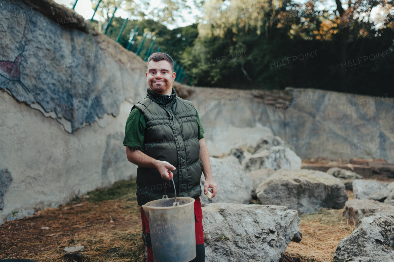 Caretaker with down syndrome in the zoo giving food in animal enclosure. Concept of integration people with disabilities into society.