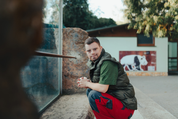 Young man with down syndrome, resting after cleaning animal enclosure in the zoo. Concept of integration people with disabilities into society.