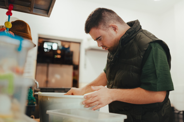 Man with down syndrome working in kitchen in a zoo, prepairing food for animals.Concept of integration people with disabilities into society.