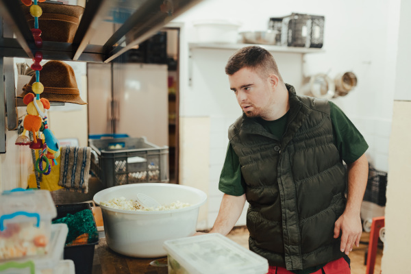 Man with down syndrome working in kitchen in a zoo, prepairing food for animals.Concept of integration people with disabilities into society.