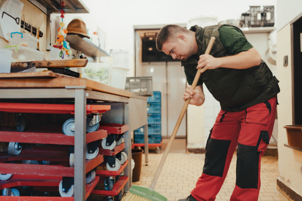 Man with down syndrome sweeping a kitchen in zoo. Concept of integration people with disabilities into society.