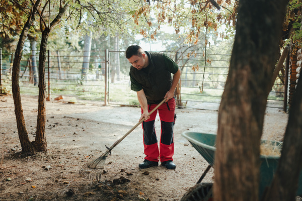 Caretaker with down syndrome in the cleaning animal enclosure. Concept of integration people with disabilities into society.